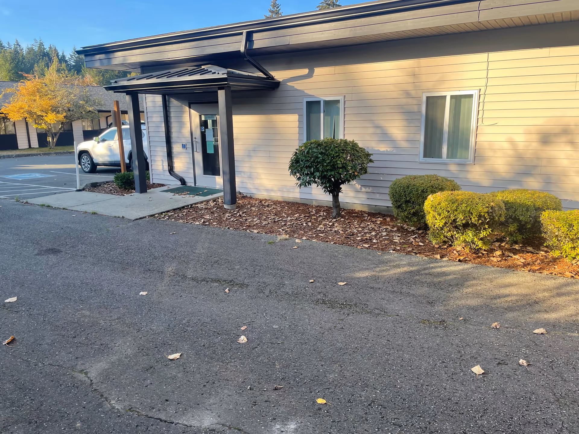 Exterior view of a senior living facility entrance with canopy and trimmed shrubs.