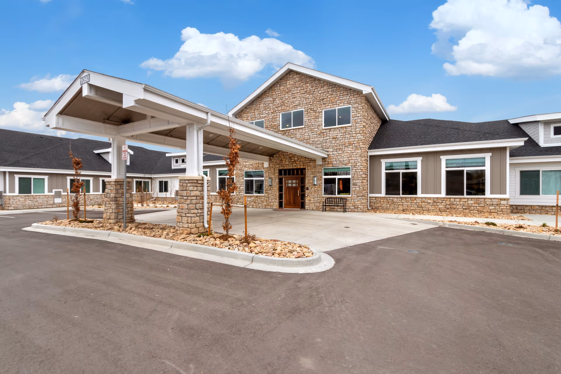Front entrance of Greeley Village senior living facility with a stone facade, covered porte-cochere, and driveway.