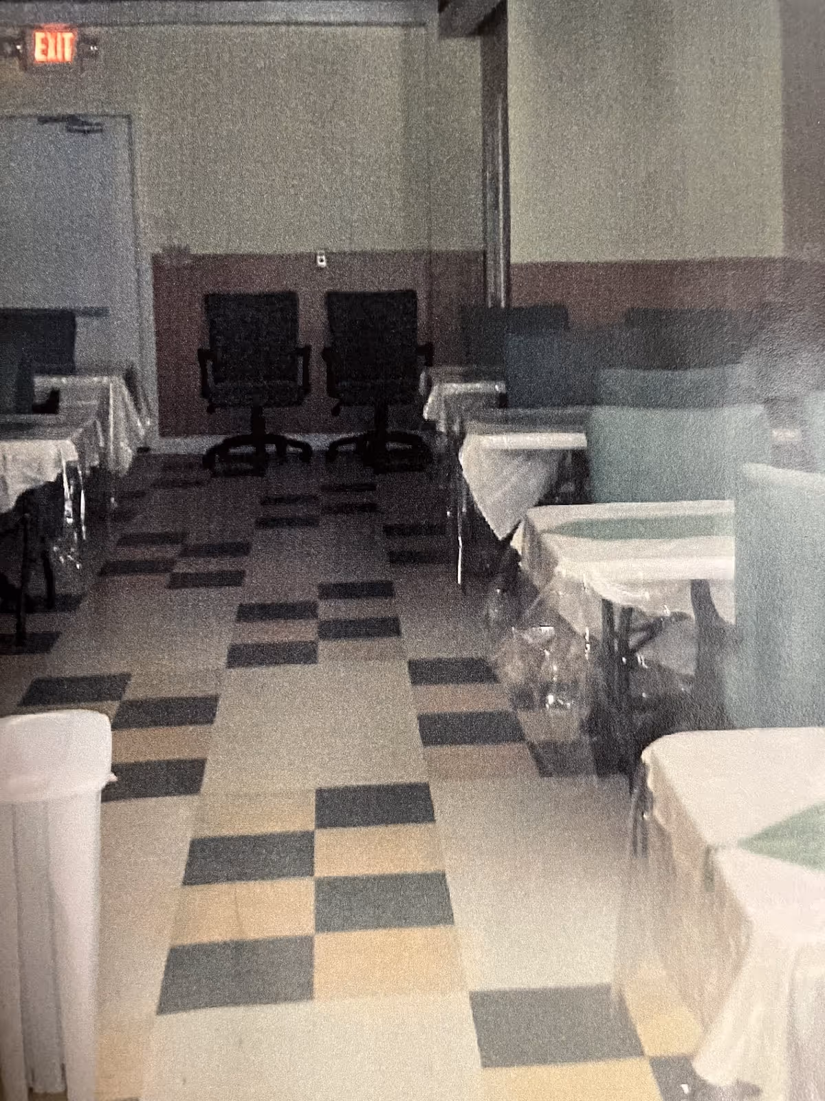 Dim interior dining room with covered tables and chairs along a checkered tile floor.