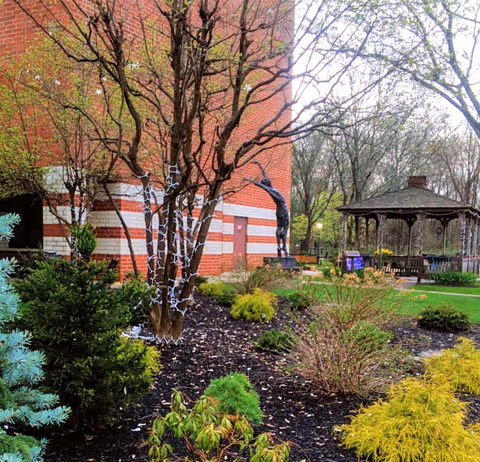 Outdoor garden area with a red brick building, string lights on trees, and a gazebo.