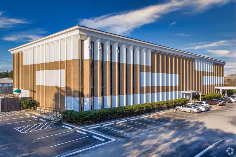 Exterior view of a modern brick-and-white facility with a parking lot in front.
