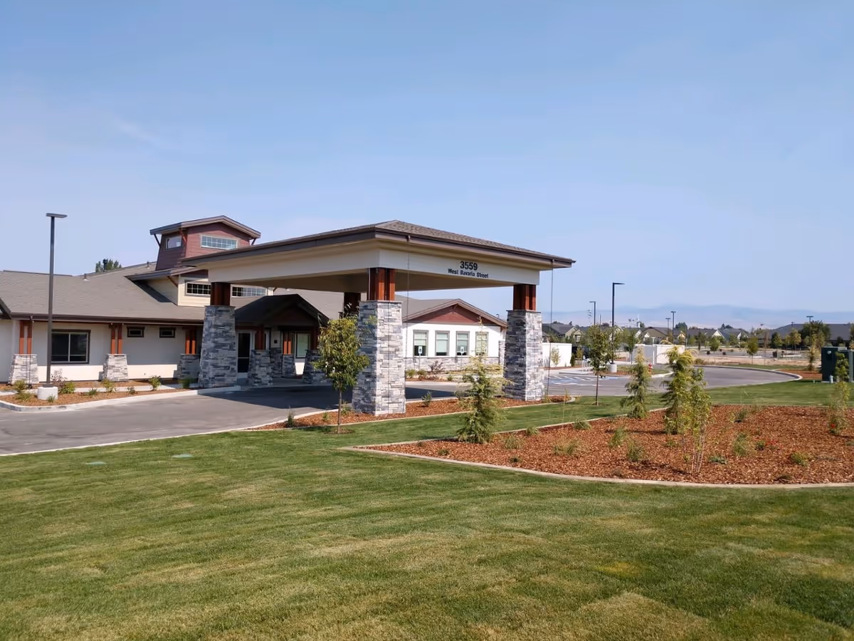 Exterior view of Table Rock Senior Living at Paramount building with a covered entrance supported by stone pillars, surrounded by a well-maintained lawn and landscaped garden beds under a clear blue sky.