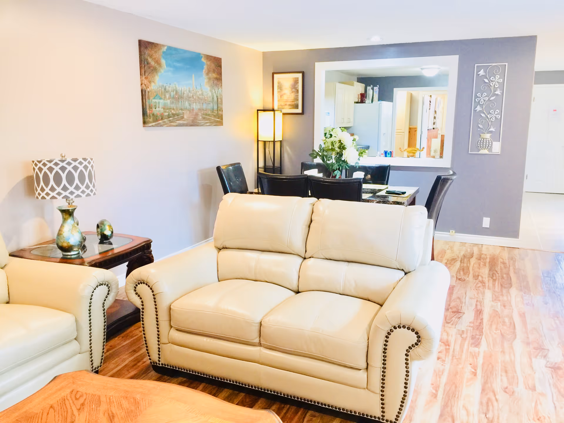 A bright living room with beige leather sofas, wood flooring, and a dining area.