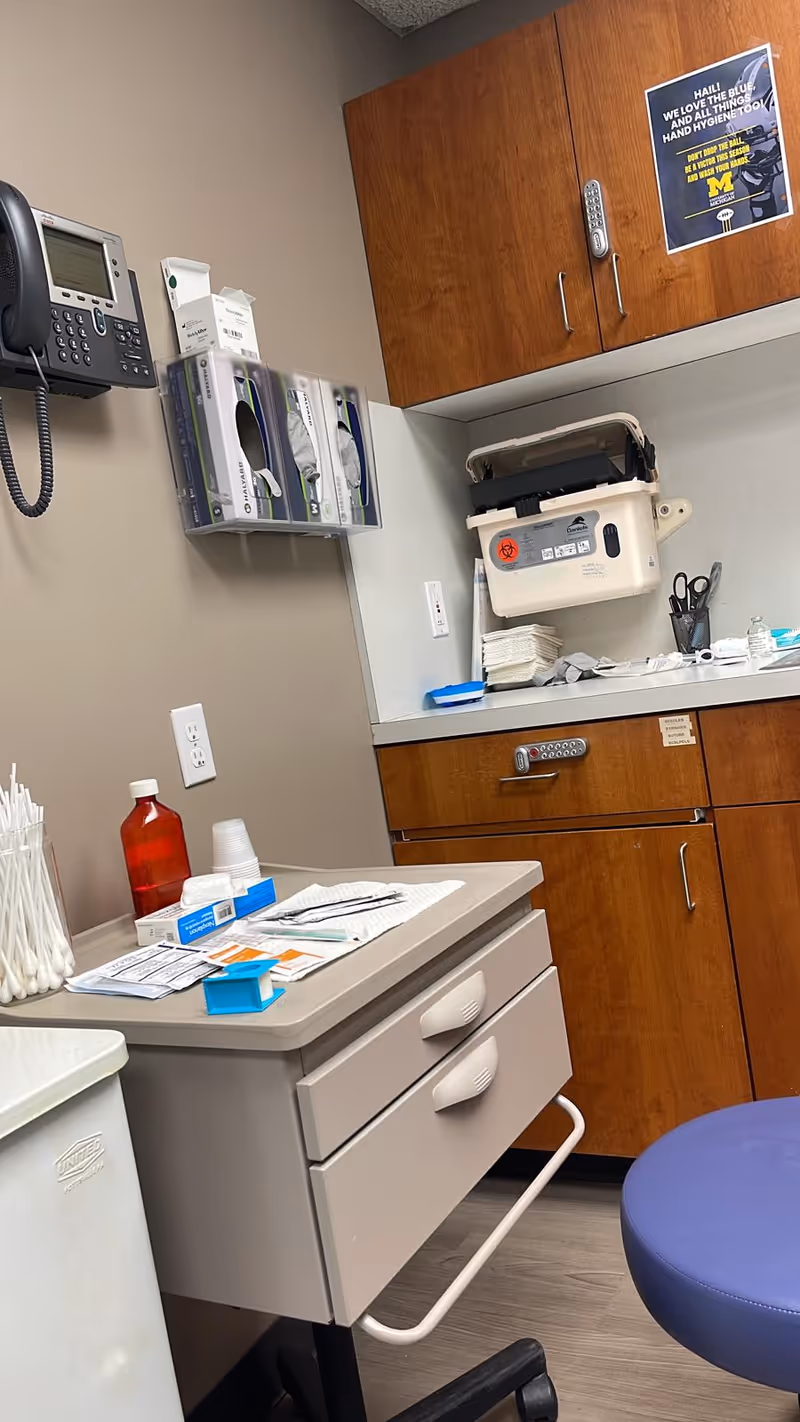Medical counter with drawers, cabinets, supplies, and a blue stool in a clinic room.