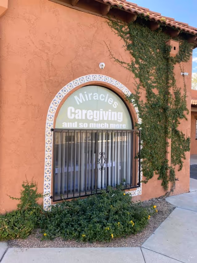 Orange stucco building with ivy, arched window, and a sign saying Miracles Caregiving and much more.