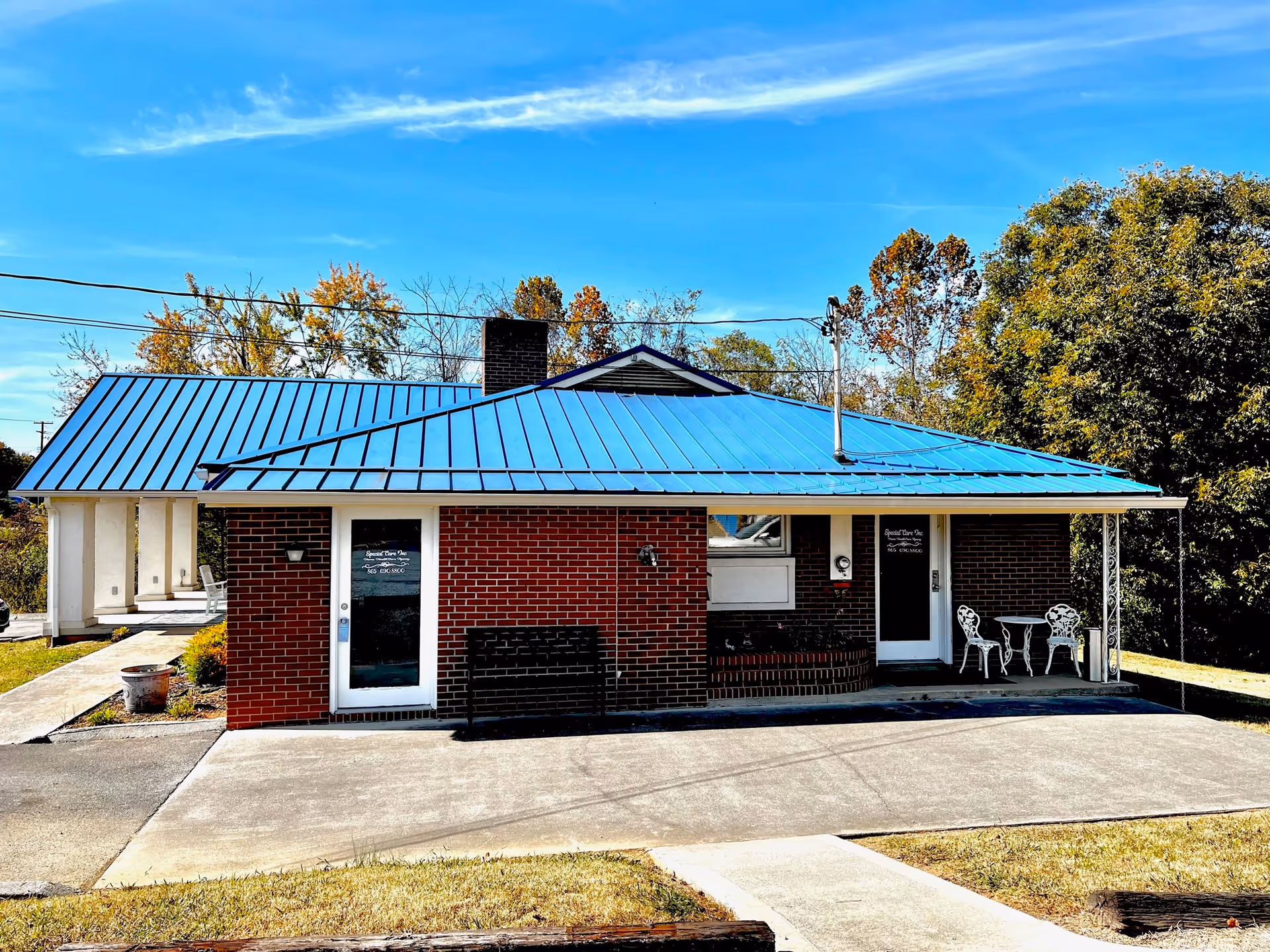 Small brick facility with blue metal roof and white outdoor seating on porch.