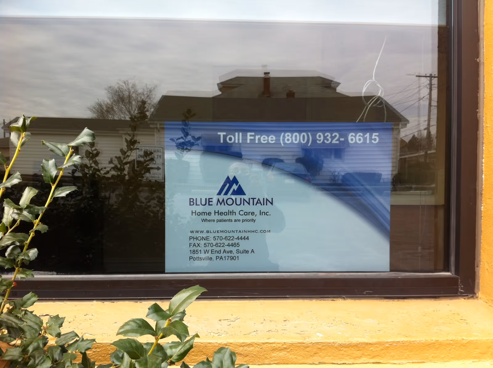 Window sign for Blue Mountain Home Health Care on yellow building exterior.
