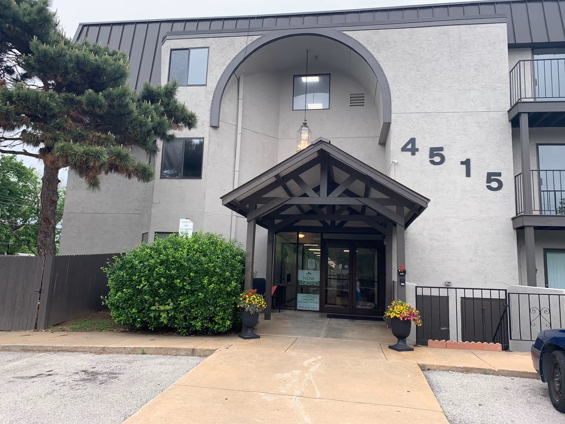 Front entrance of a multi-story retirement community building with a covered entry, address numbers "4515", planters, and greenery.