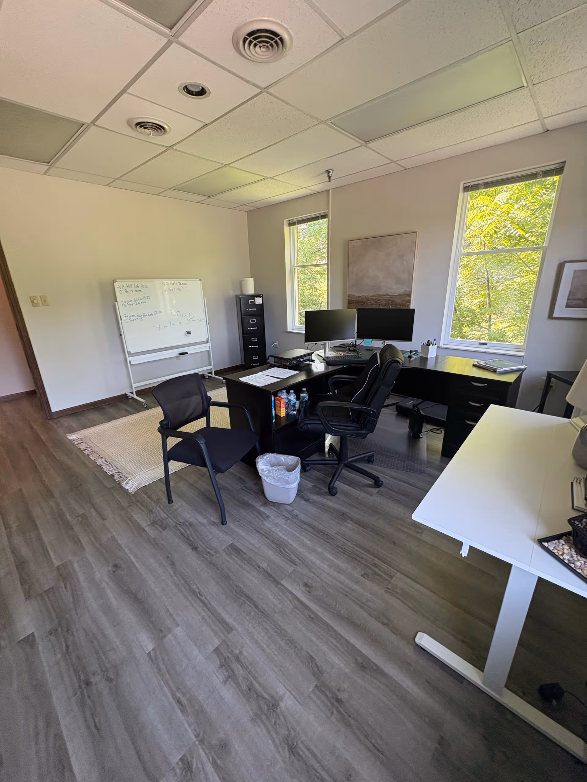 Administrative office area in a senior living facility with desks, monitors, a whiteboard, and windows.