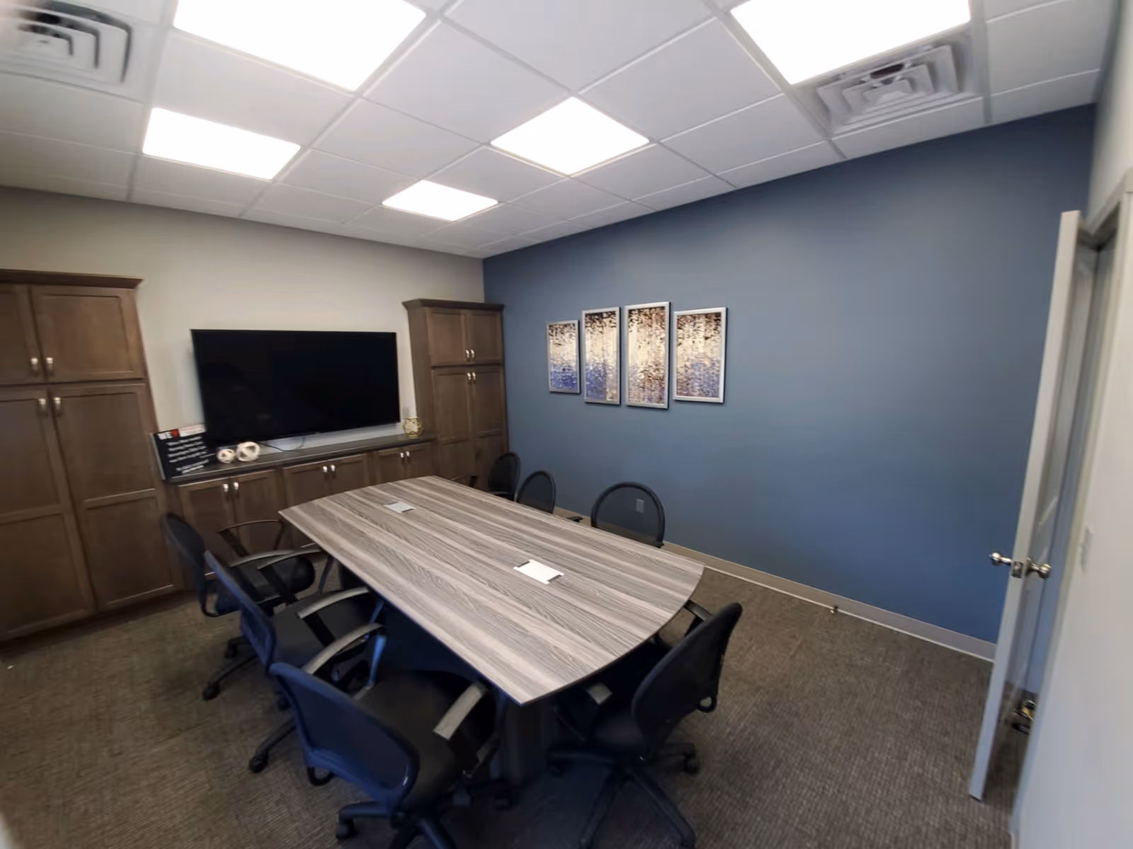 A conference room with a long table, chairs, cabinets, and a wall-mounted TV.