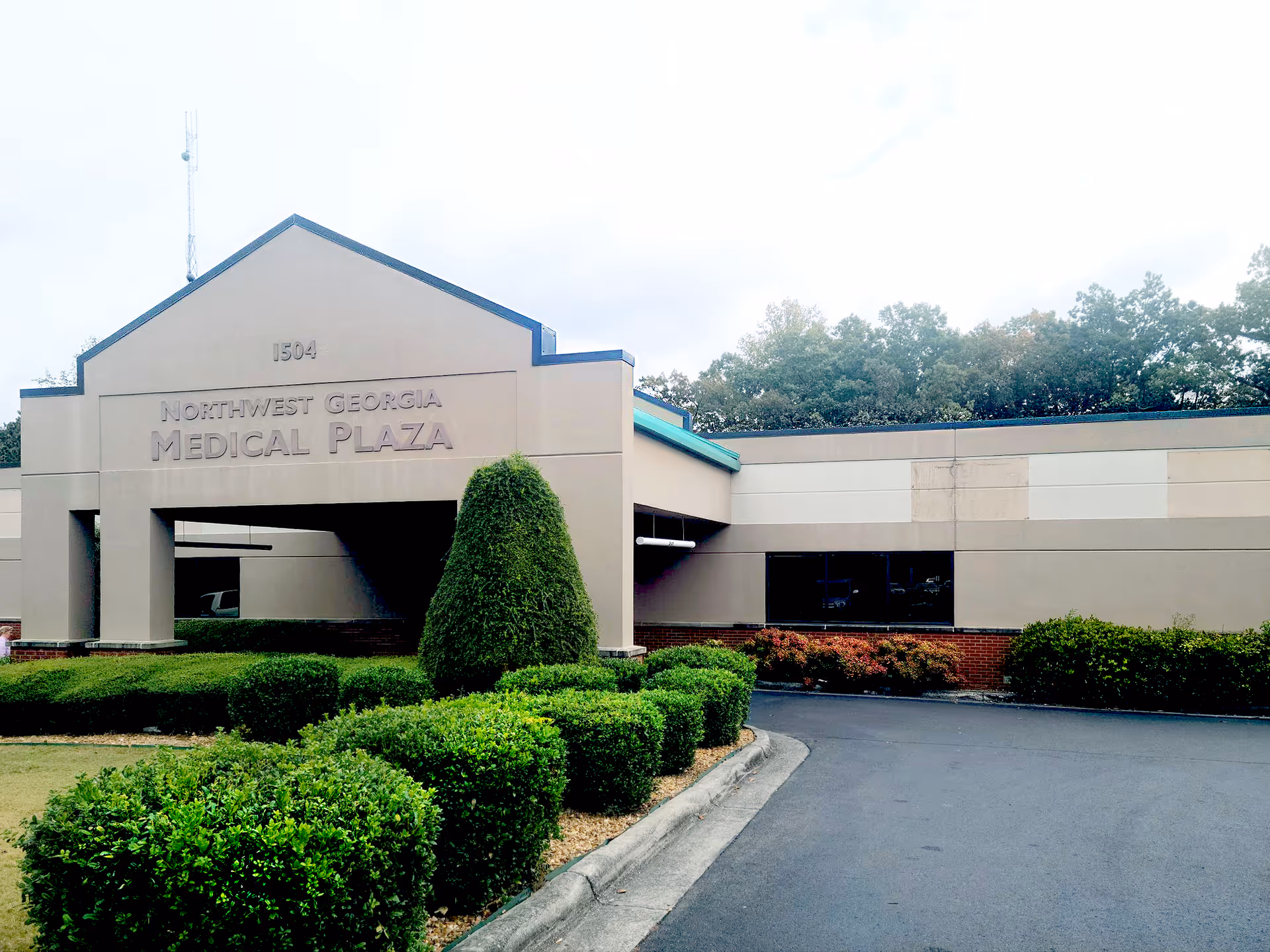Exterior view of a beige medical plaza with manicured shrubs and sign.