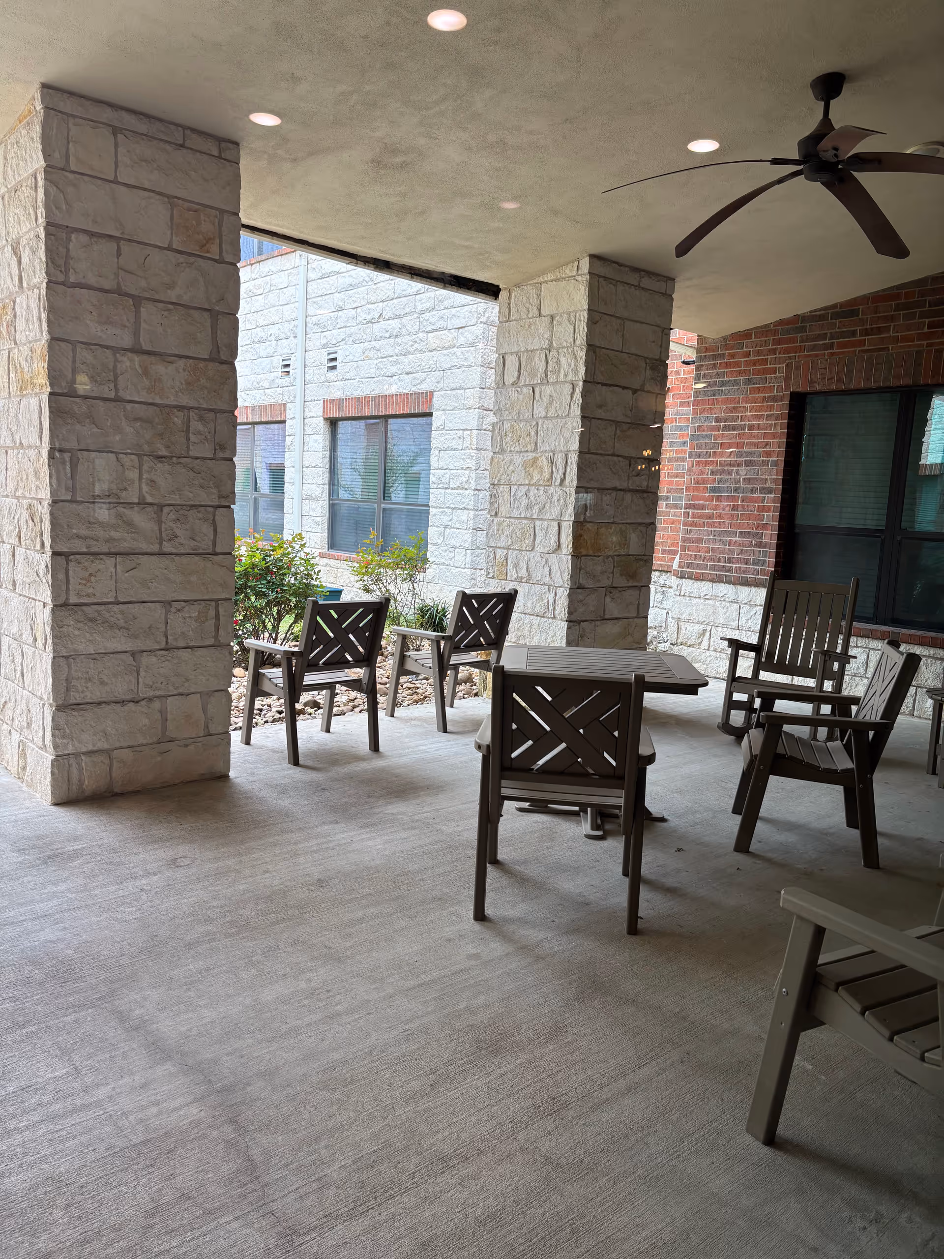 Covered outdoor patio with wooden chairs and tables around stone columns.