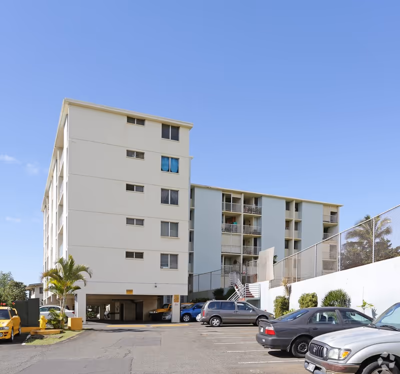 Exterior view of a multi-story senior living building with parked cars and palm trees.