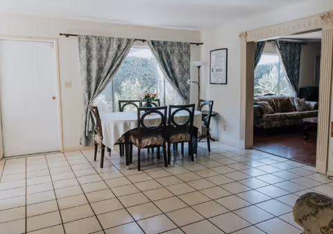 A tiled dining area with a table set for six near large windows and curtains.