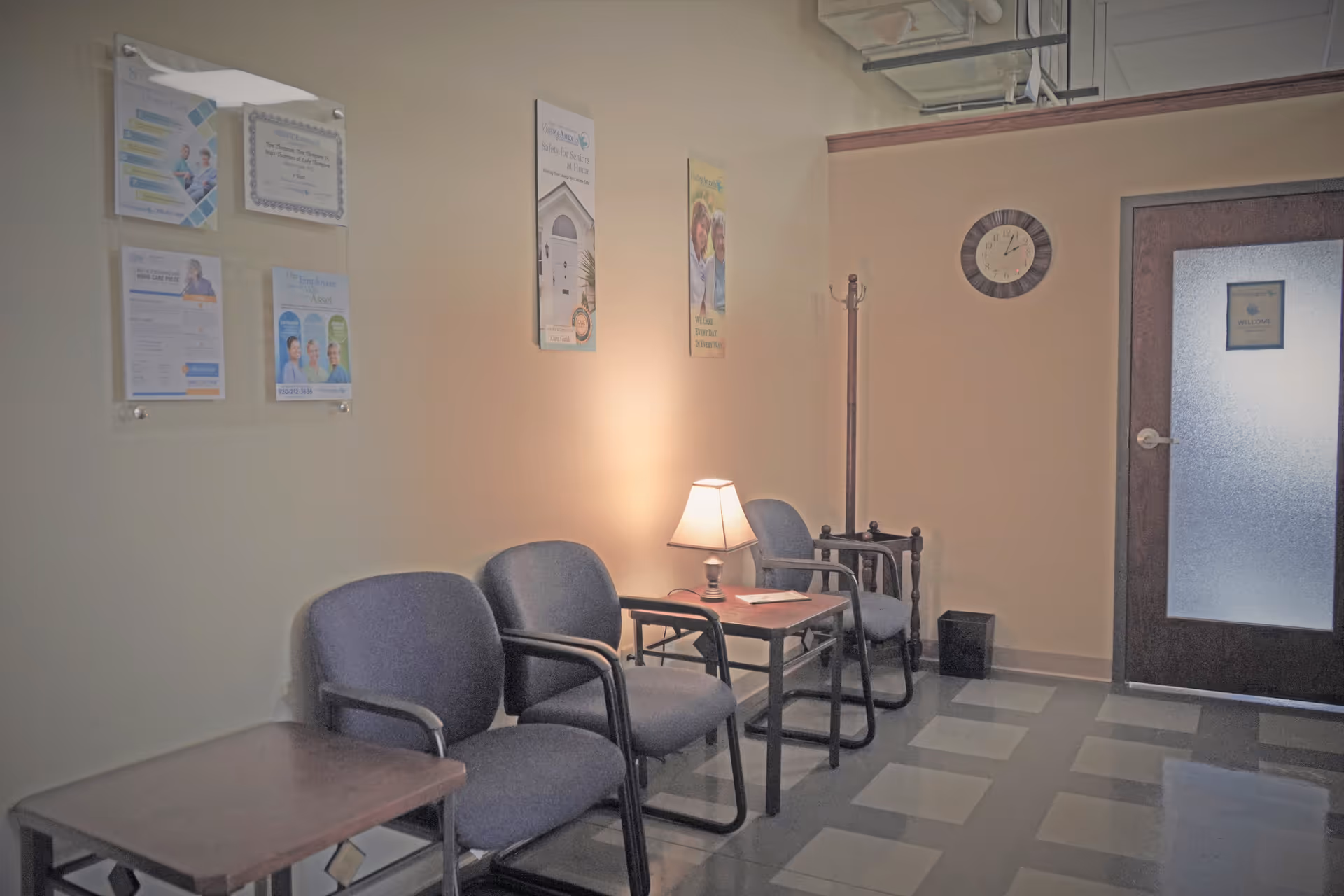 A small lobby with chairs, a table lamp, posters, and a frosted door.