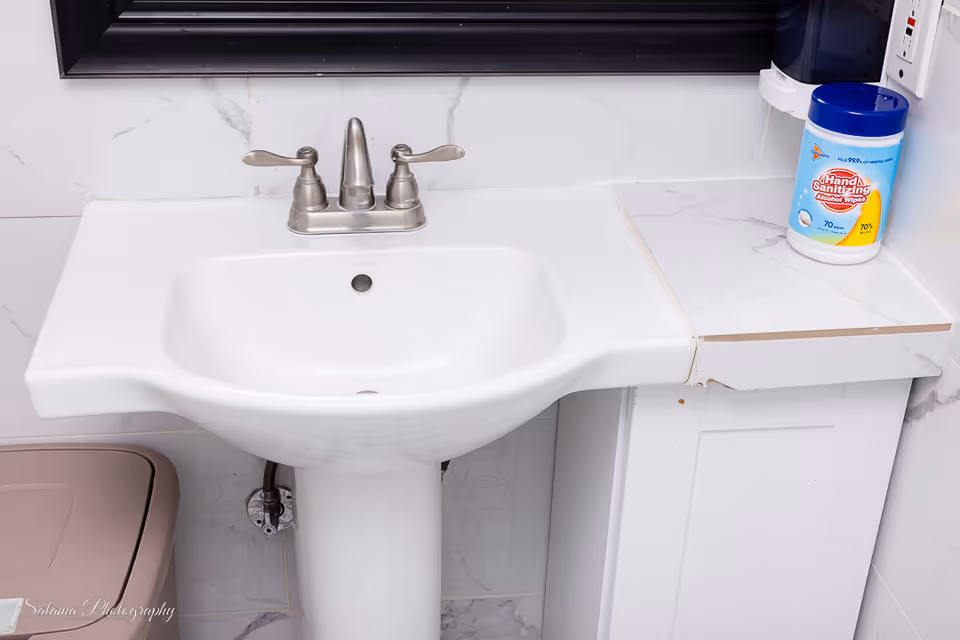 White bathroom sink with faucet, marble countertop, mirror, and hand sanitizer bottle.
