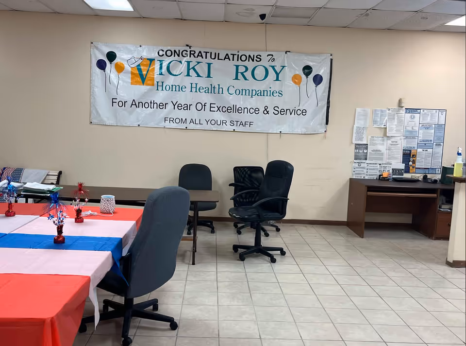 An indoor facility room featuring a congratulatory banner, tables with patriotic tablecloths, and an office desk.