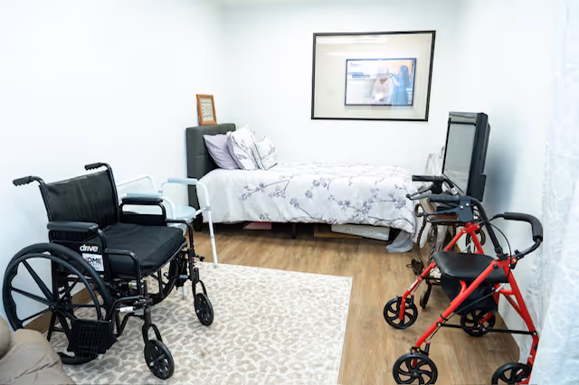 Bedroom in a senior facility with a bed, wheelchair, walker, and television.