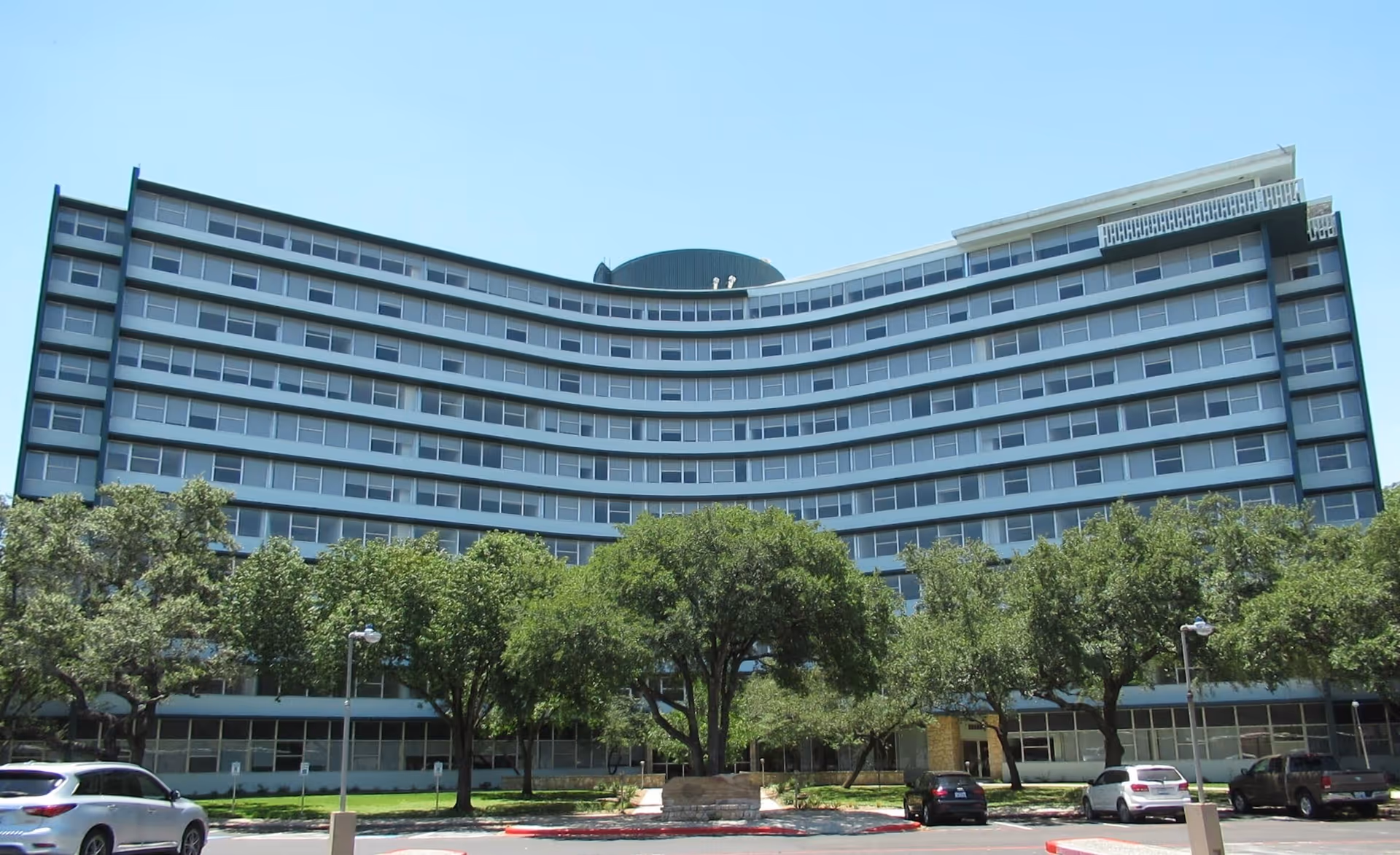 Curved, multi-story senior living building with trees and parked cars.