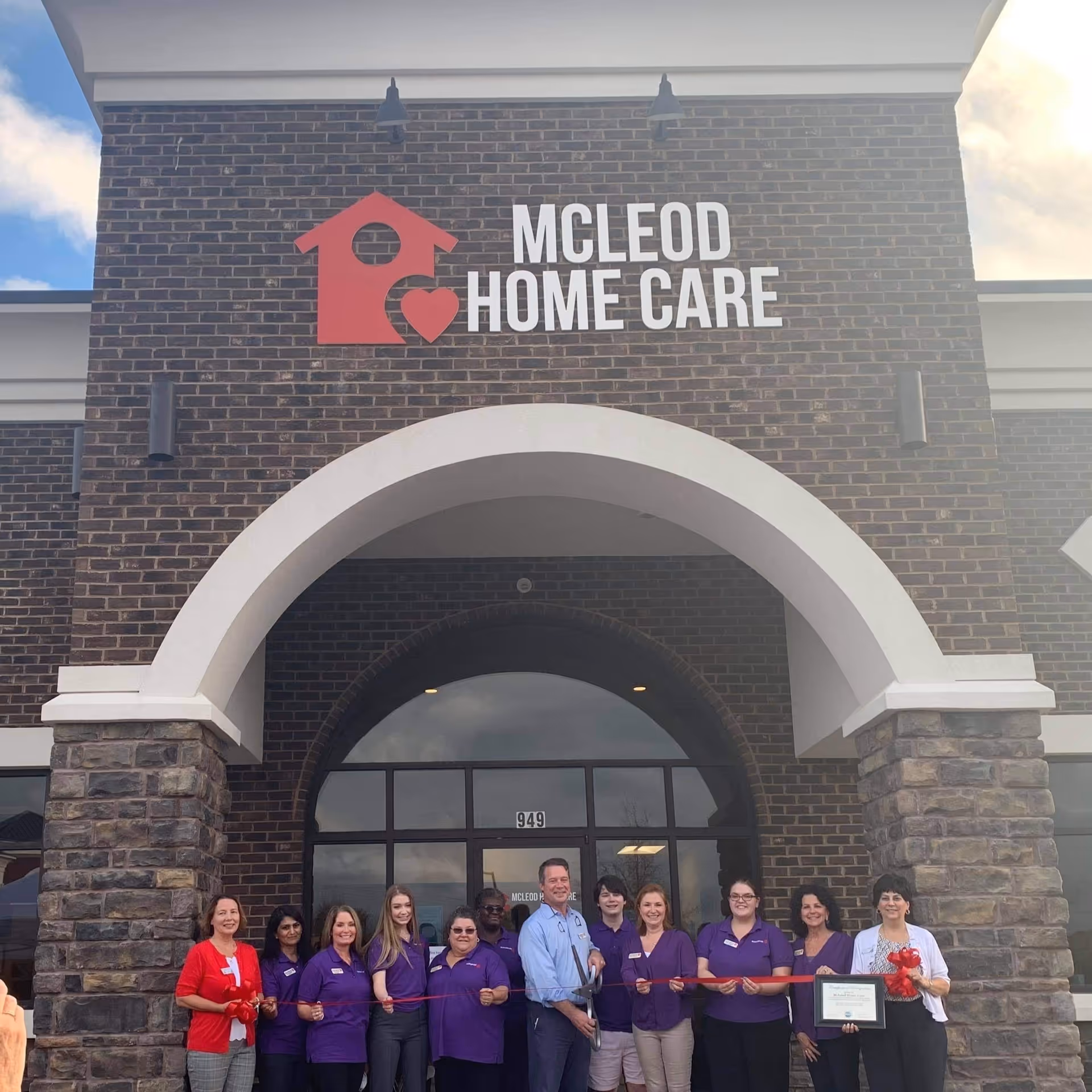 Group of staff stands in front of McLeod Home Care facility with ribbon-cutting ceremony.