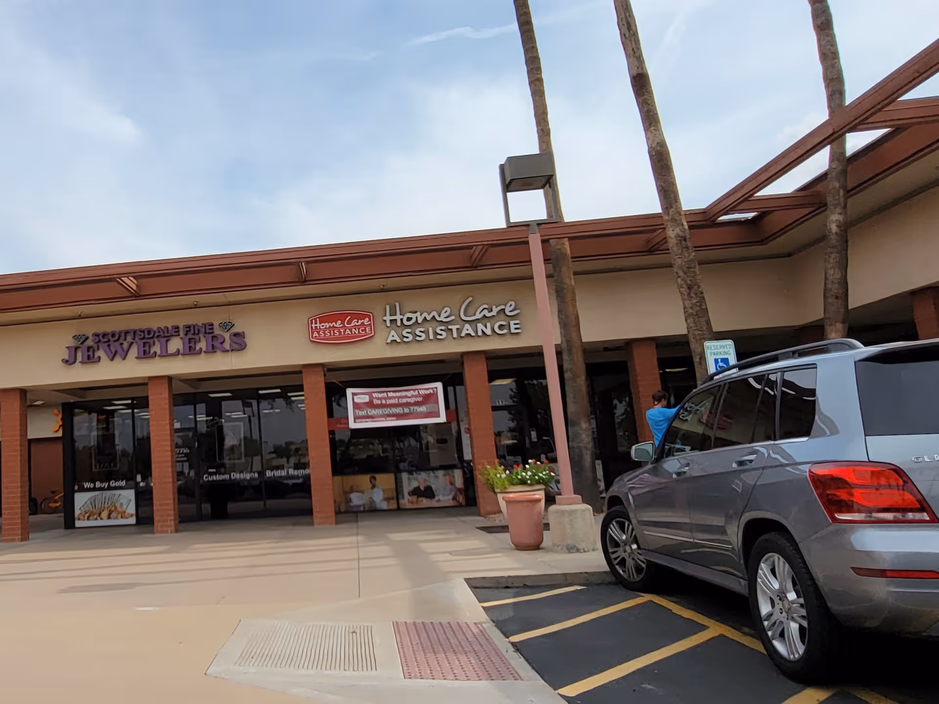 Exterior view of a shopping plaza with storefronts and a parked silver SUV