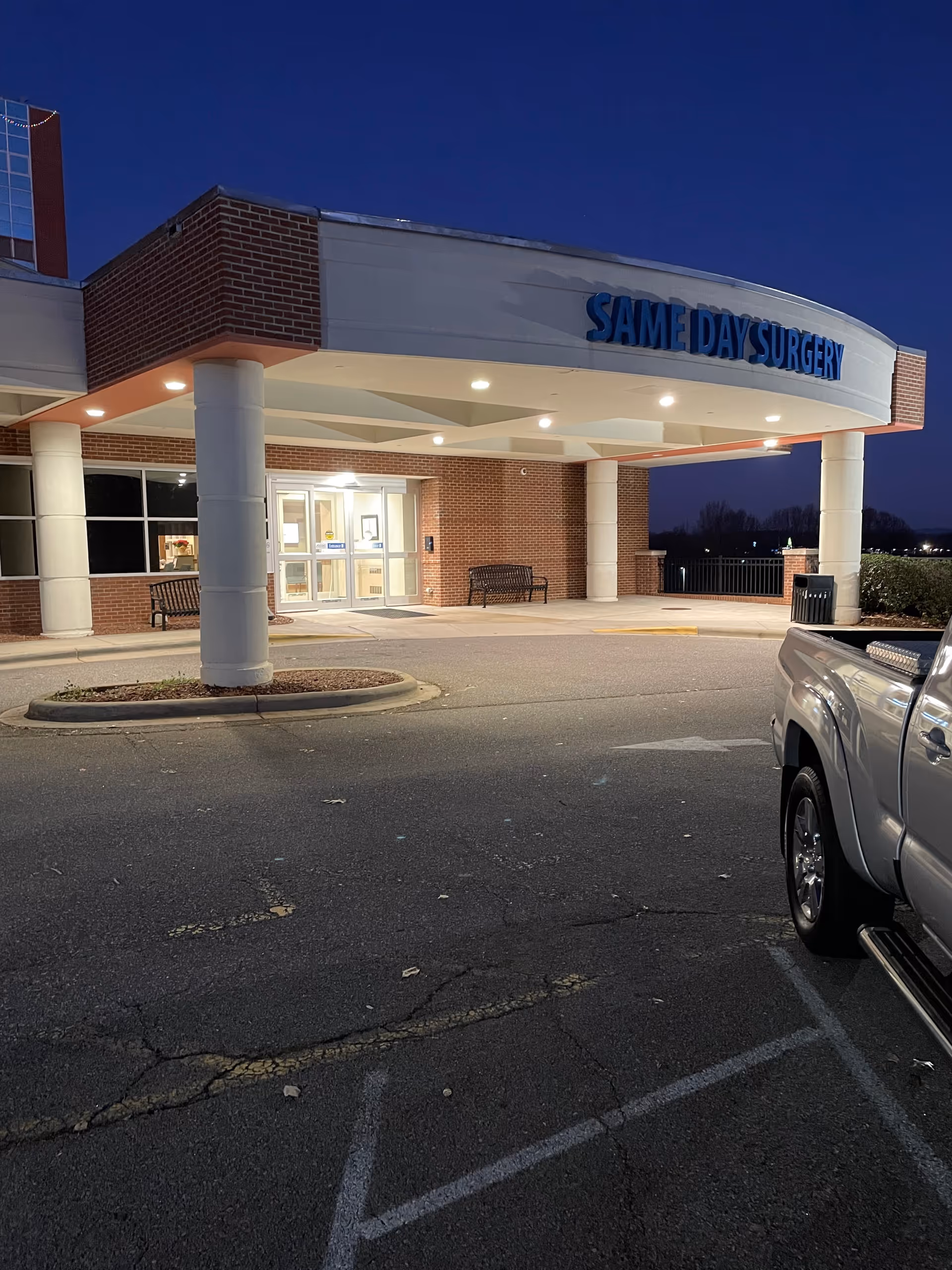 Exterior view of a brick medical facility entrance with columns and a parking lot.