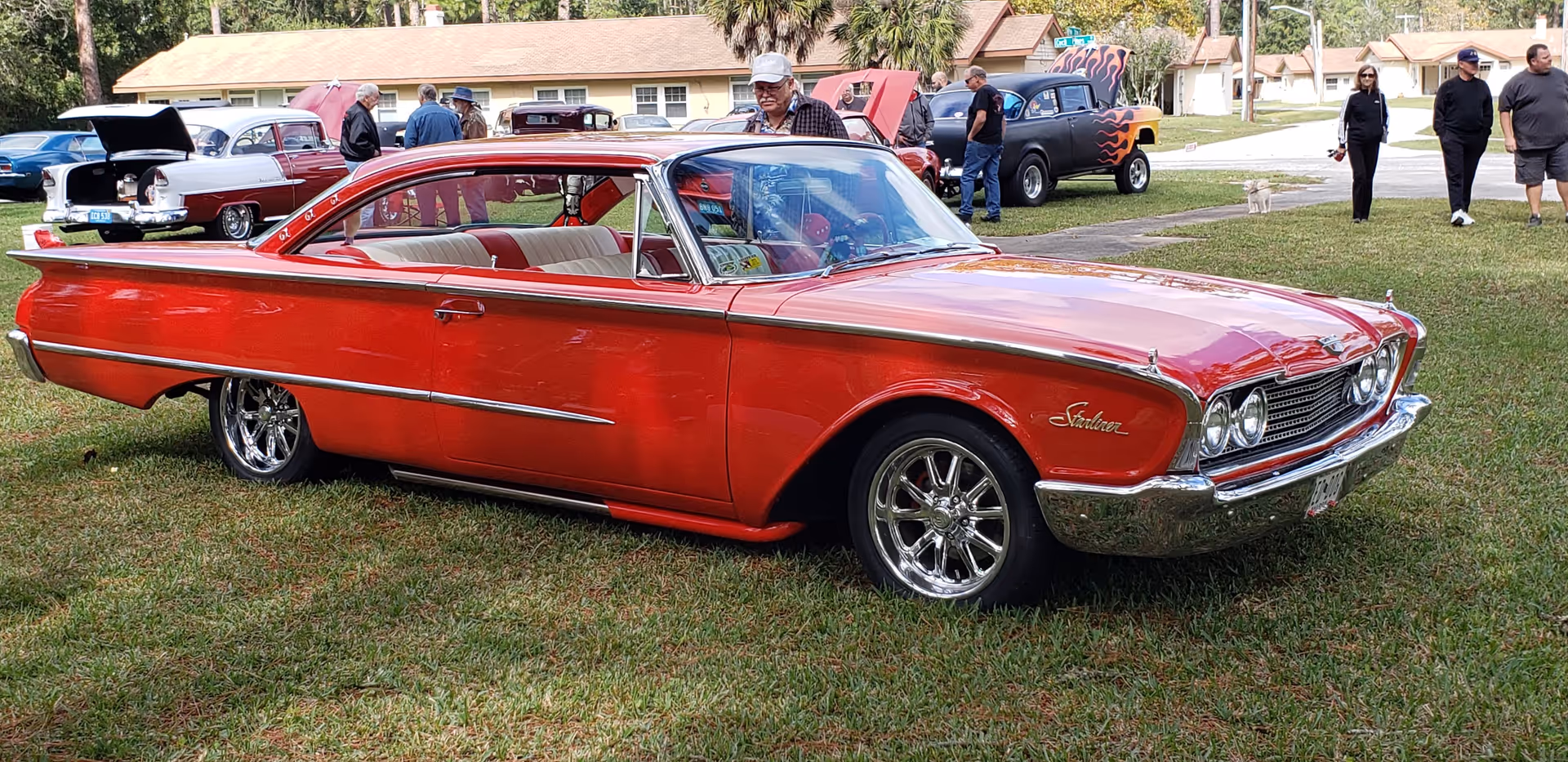 A bright red vintage car parked on a grassy field at a car show.