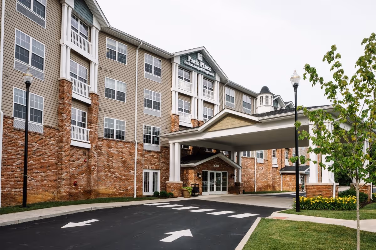 Front entrance of a multi-story senior living building with a covered porte-cochère, brick facade, and a sign reading Park Place at Winghaven.