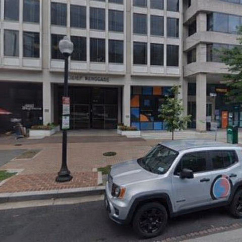 City street view of a modern building entrance with a parked SUV.
