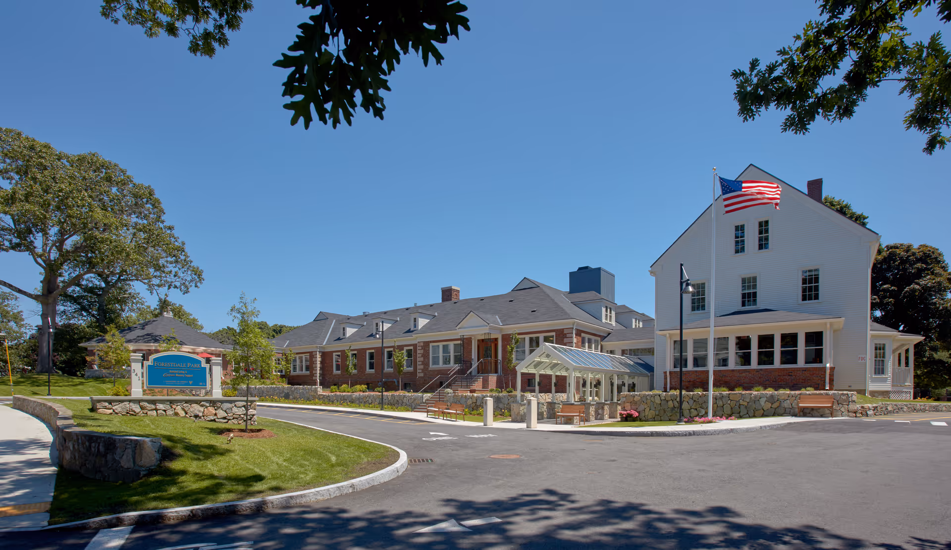 Exterior view of Forestdale Park Senior Living with flag, sign, and driveway.