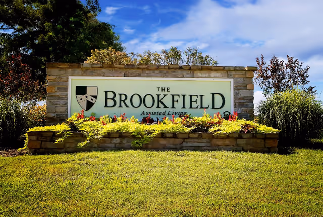 A stone sign reading 'The Brookfield Assisted Living' with colorful mulch and plants.
