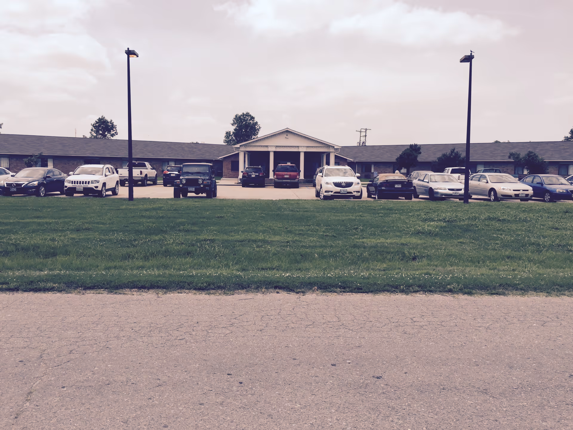 Single-story care facility with a front entrance and a row of parked cars.