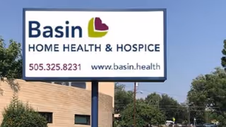 Outdoor sign for Basin Home Health & Hospice with a building and trees nearby.