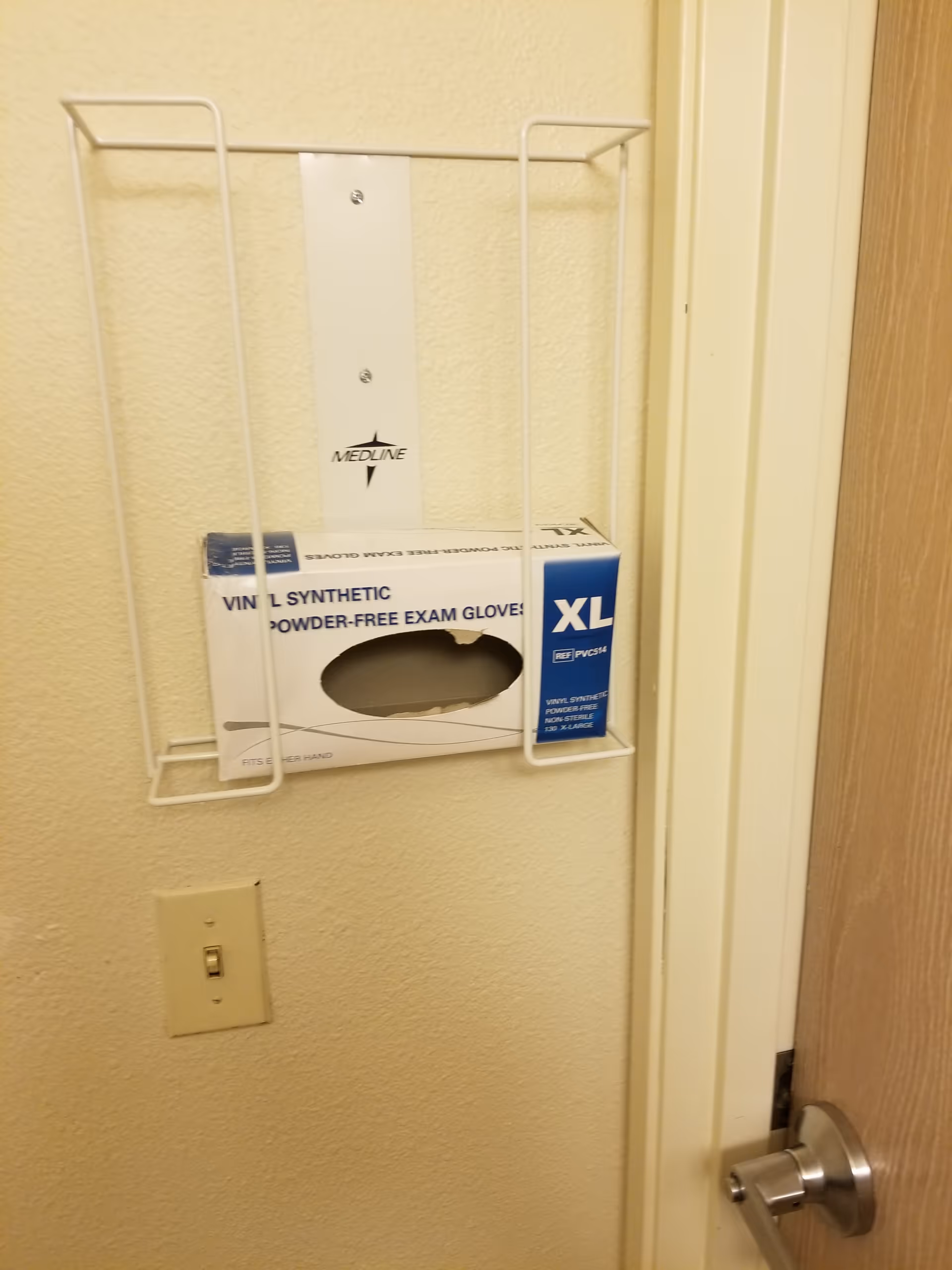 Wall-mounted glove box holder with disposable gloves in a hallway.