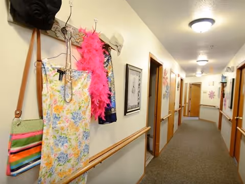 Interior hallway of Azura Living with coats, bags, a pink feather boa, and framed art.