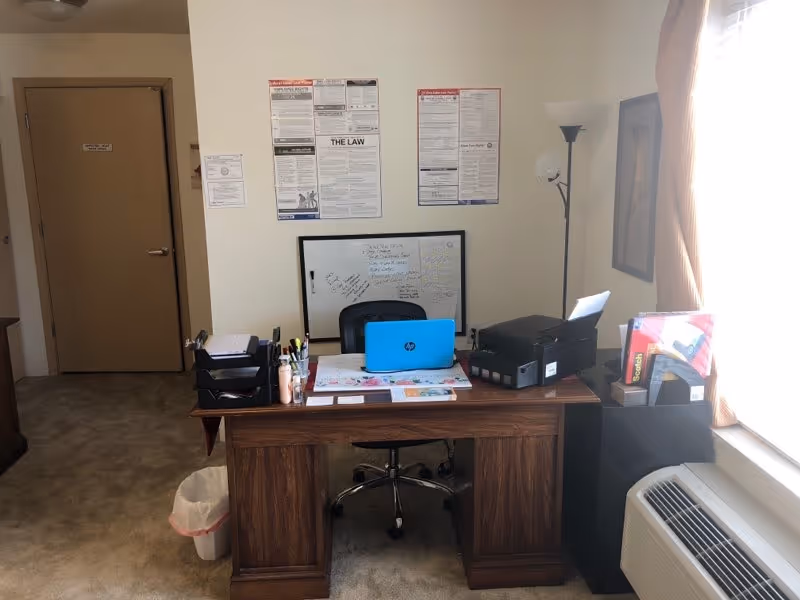 Interior office desk with supplies, printer, laptop, and wall charts.