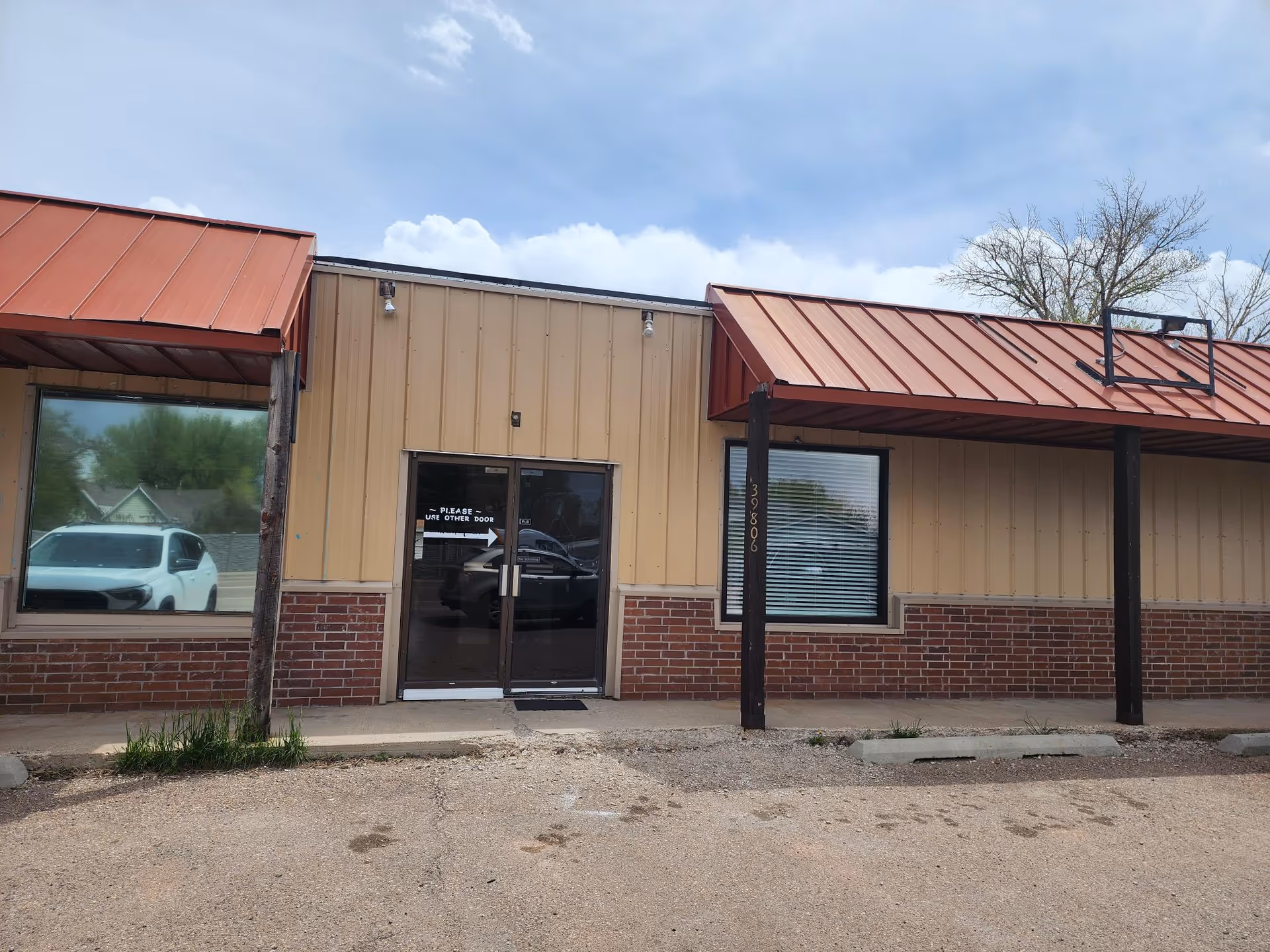 Front exterior of a single-story building with brick base and red metal awnings.