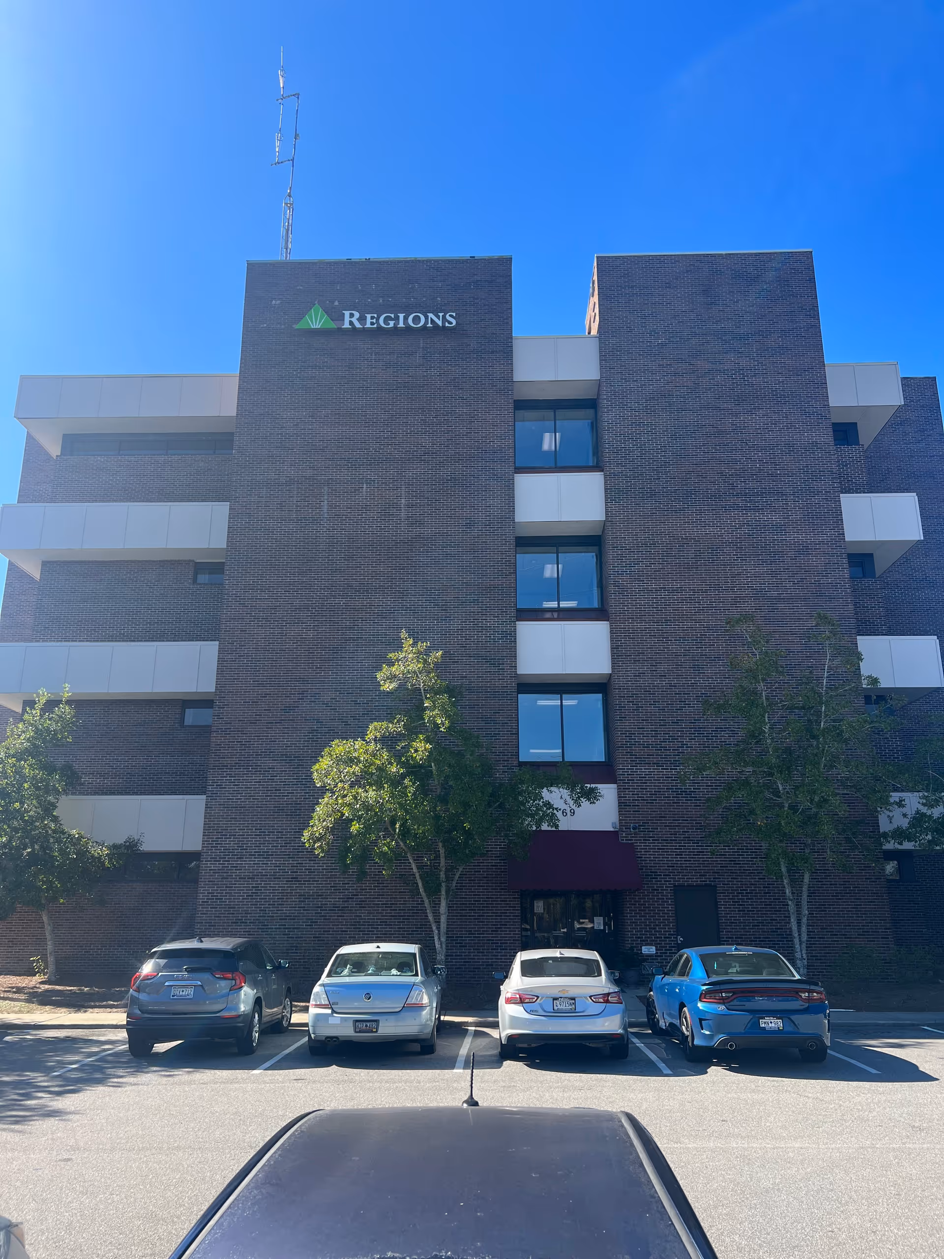 Brick multi-story building with Regions sign, parked cars, and clear blue sky.