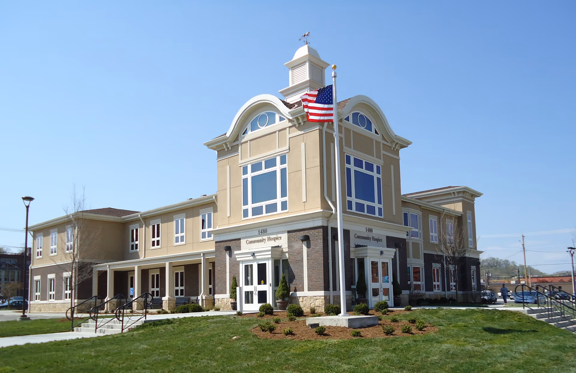 Exterior view of a beige Community Hospice building with flagpole and entrance.