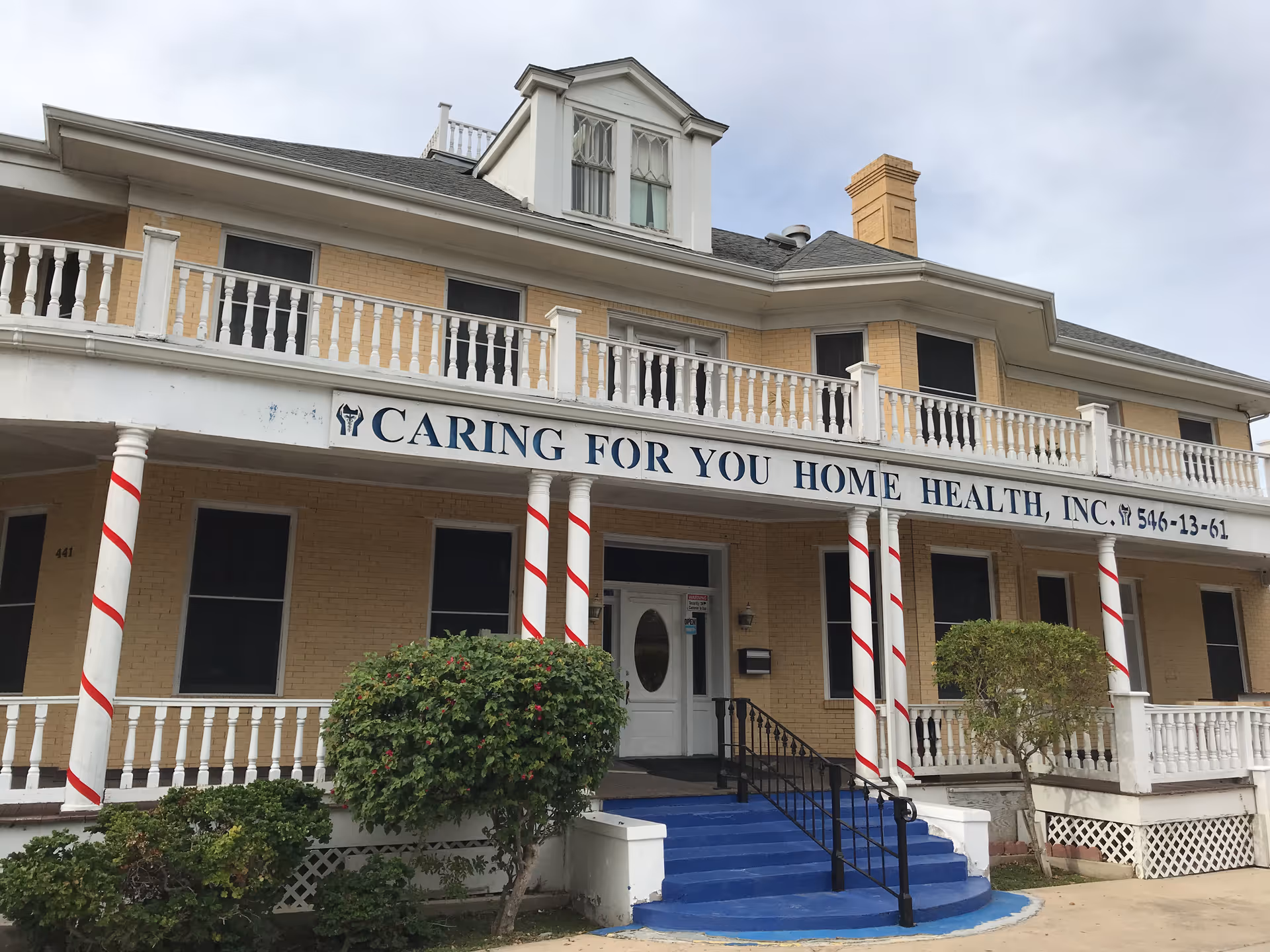Two-story brick building with wraparound porch and striped columns.