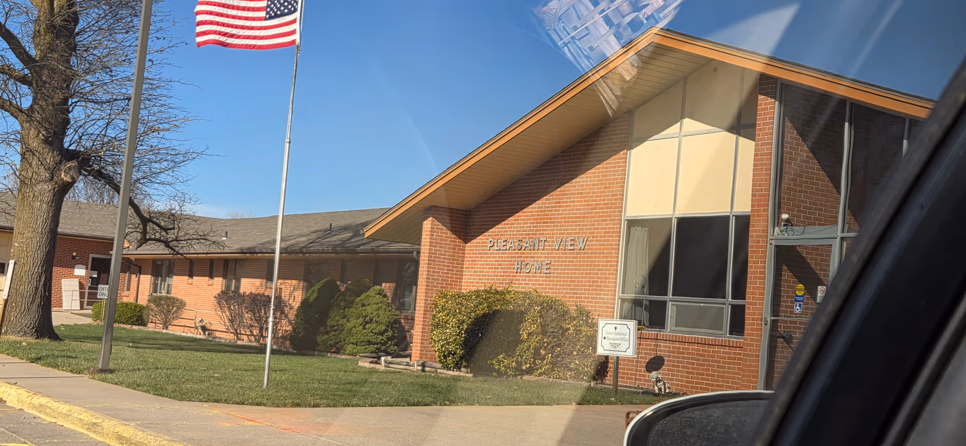 Pleasant View Home exterior: brick building with entrance, flagpole, and manicured shrubs.