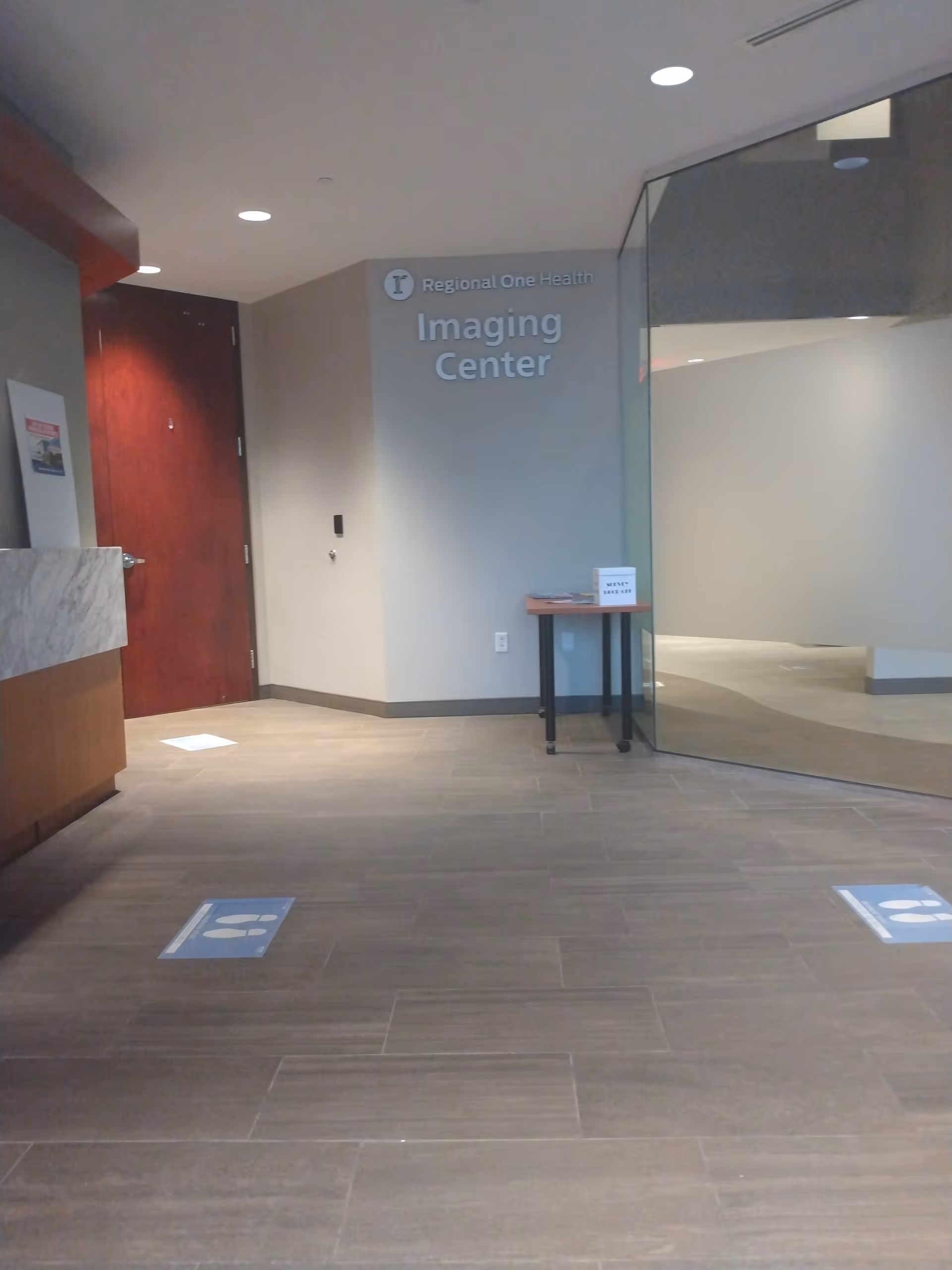 Interior hospital hallway leading to the Imaging Center with glass walls and a small table.