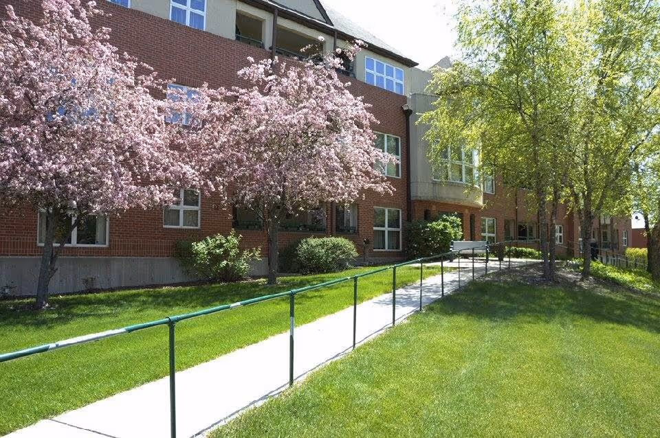 Exterior view of Valley View Village with brick building, ramp, and blossoming trees along walkway.