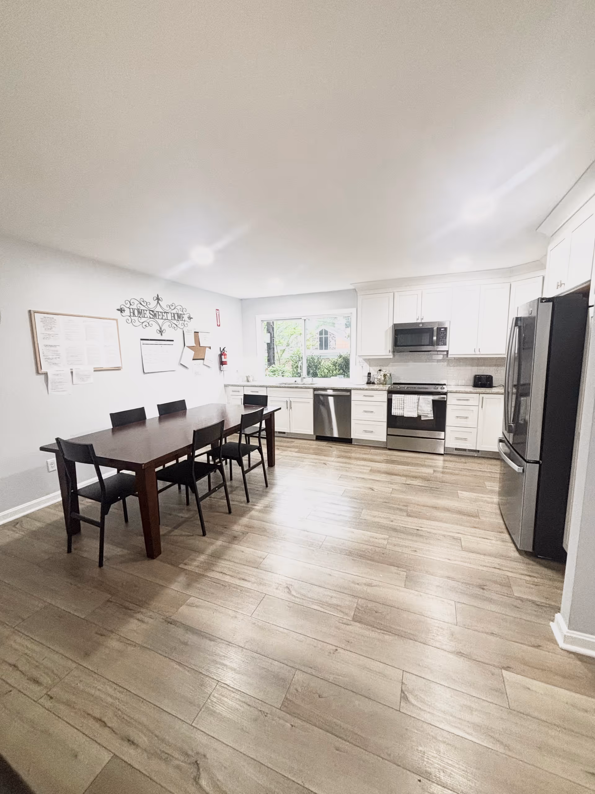 Bright dining kitchen area with white cabinets, stainless appliances, and a long dining table.
