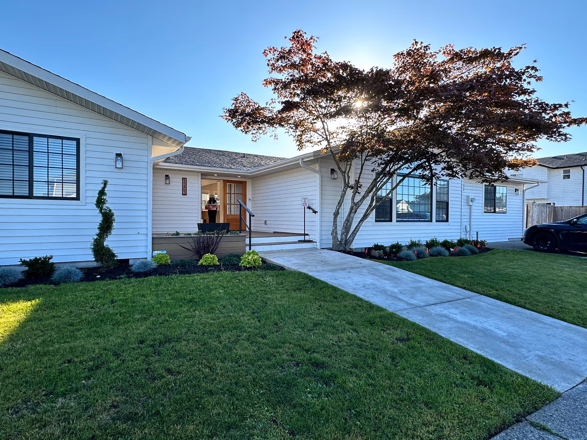 Front exterior view of a single-story white care home with walkway and landscaped lawn.