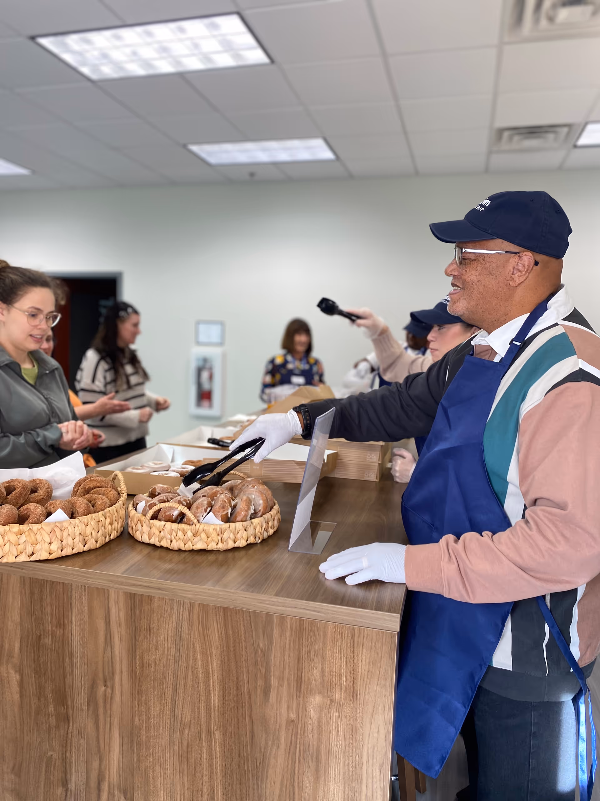 Staff member in apron serves donuts from baskets at a counter while guests wait.