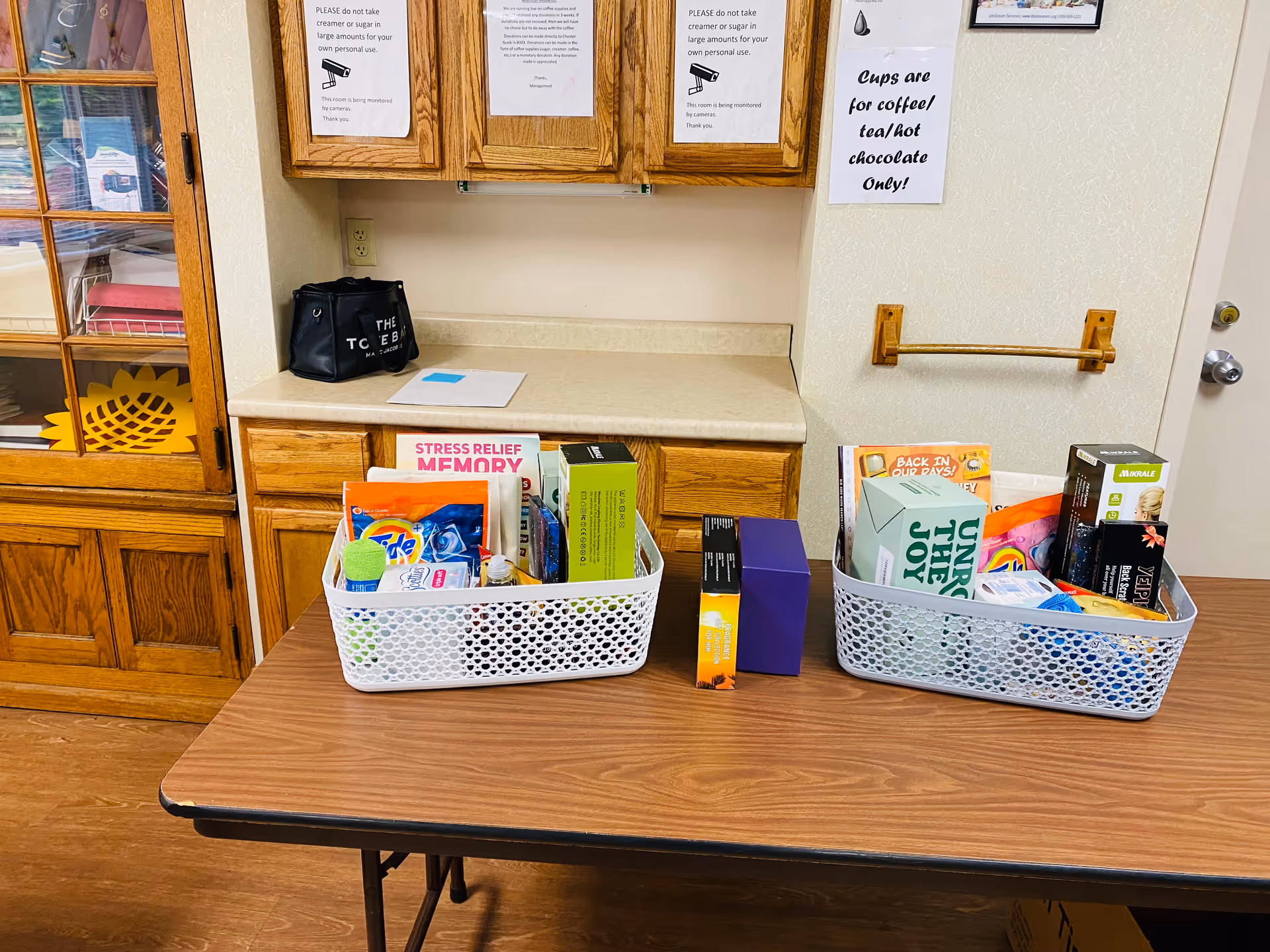 Two white mesh baskets filled with assorted items sit on a wood table in cabinet-filled room.