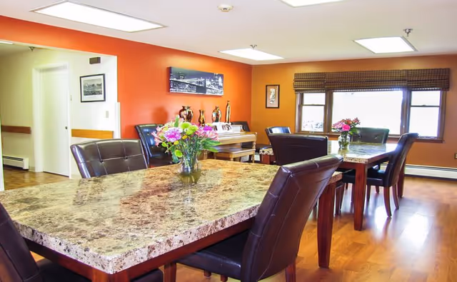 Bright senior living dining area with marble-top tables and floral centerpieces.