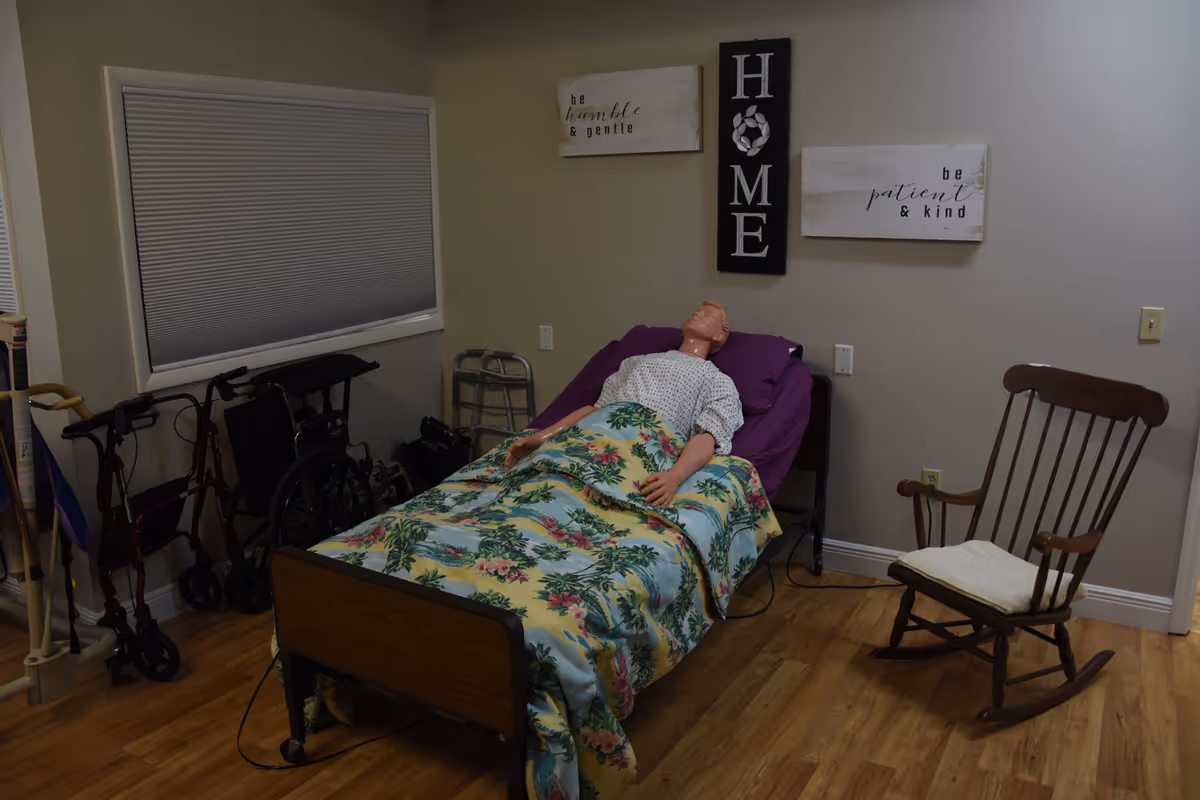 A care room with a hospital bed, walker, and rocking chair in a beige space.