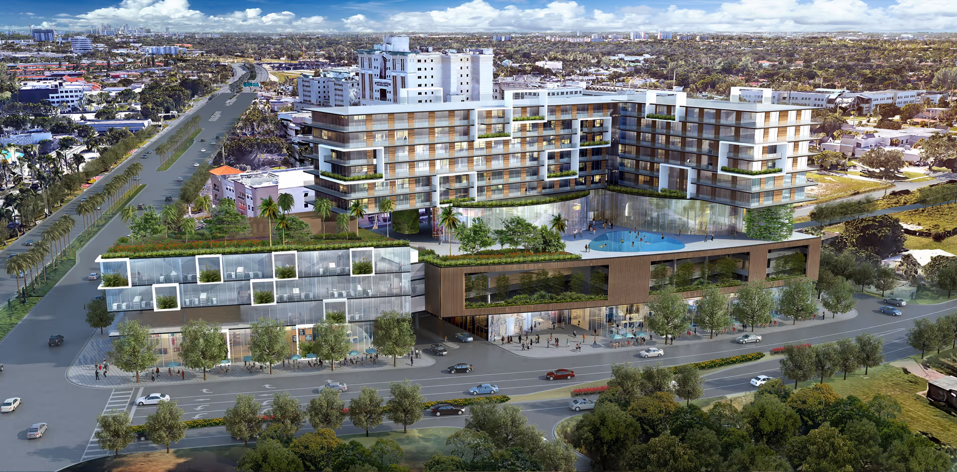 Aerial view of a modern multi-story senior living facility named The International at Aventura Senior Living, featuring a large building with glass windows, balconies with greenery, a rooftop pool, and surrounding roads with cars and trees.